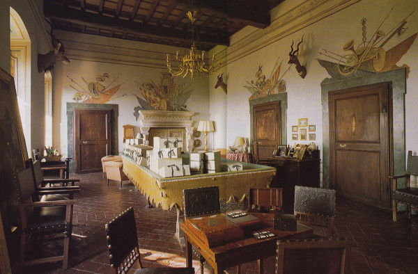 In a photo taken in the 1980's by James Mortimer boxes tied with ribbons containing archival papers on the history of the palazzo are piled on the billiard table. Spears, trumpets and standards are painted above the doors and mantelpiece. On the walls are heads of game shot by Arabella Lennox-Boyd - for food - when on a safari in Africa. 